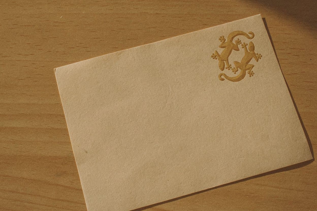 Sobre de papel color arena sobre madera clara, con el sello de los dos lagartos estampado en dorado