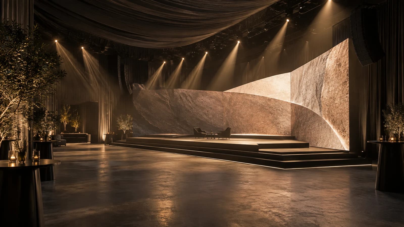 Haces de luz cálida caen desde el techo sobre un escenario escalonado con pantallas de textura pétrea.